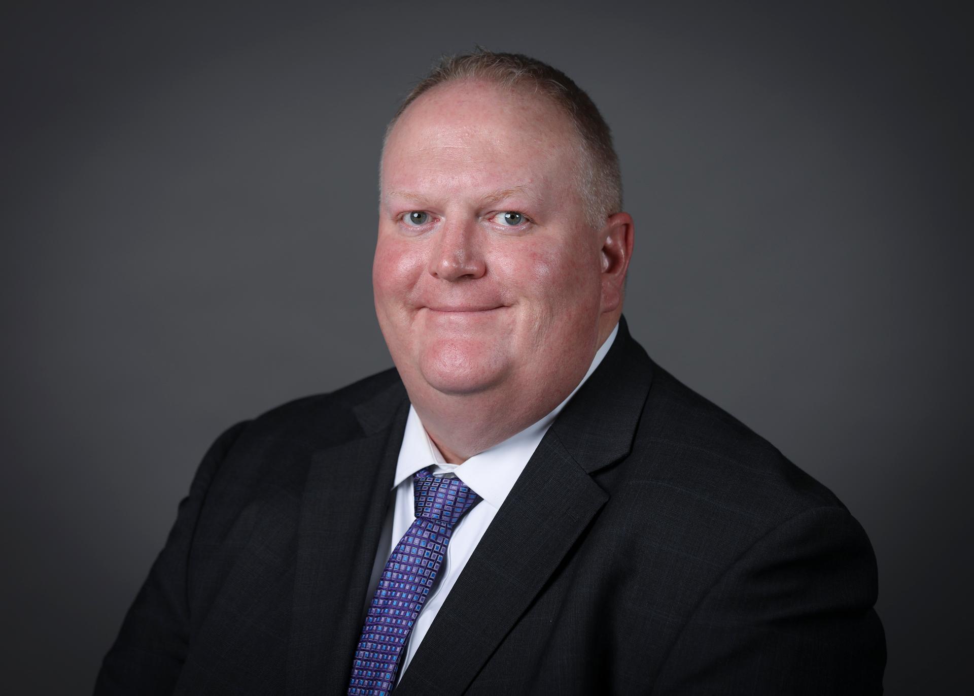 Man in suit and tie in front of grey background.