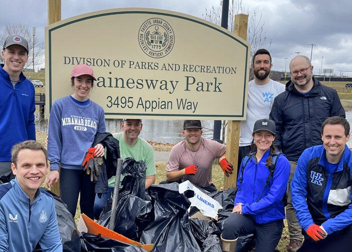 Volunteers pose next to a sign at Gainesway Park after picking up litter with bags and grabbers